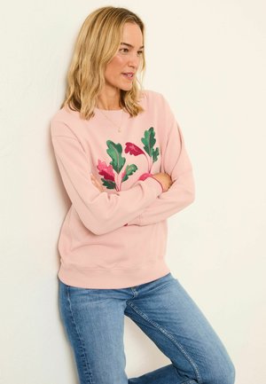 Jasnoróżowa bluza z nadrukiem kwiatowym w odcieniach zieleni i czerwieni. Okrągły dekolt, długie rękawy, prążkowane mankiety, zestawiona z niebieskimi dżinsami.