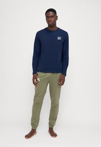 Chemise à manches longues navy avec un petit logo brodé, assortie à un pantalon de jogging vert olive ; les deux sont fabriqués dans un tissu léger et doux.