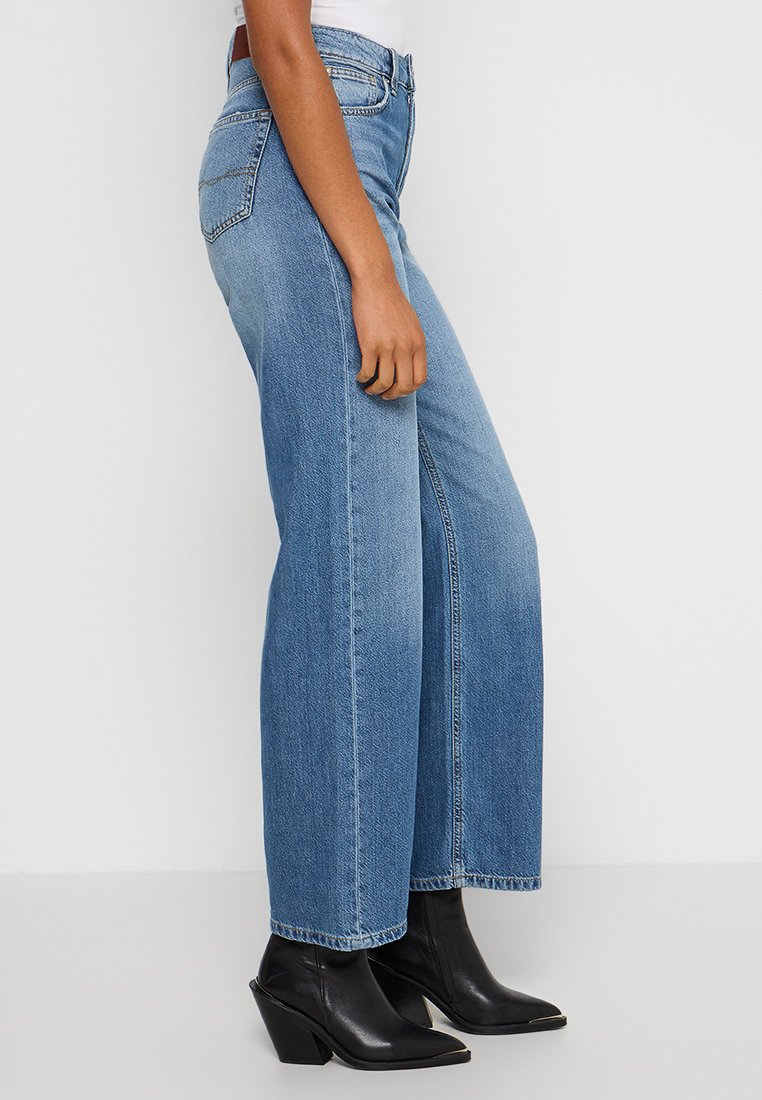 Jasnoniebieskie dżinsy w szerokim kroju z klasycznego materiału dżinsowego, z wysokim stanem i czystym wykończeniem, w połączeniu z czarnymi botkami za kostkę.