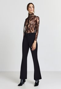 Maglia a maniche lunghe a fantasia marrone e nera con collo alto, abbinata a pantaloni neri svasati e stivaletti neri con tacco.