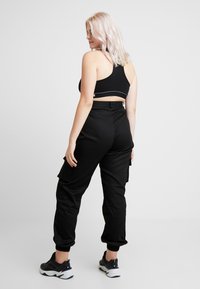 Svart kortad sport-bra och svarta cargobyxor med elastiska muddar. Mjuk tyg med sidofickor och minimalistisk design. Svarta sneakers fulländar looken.