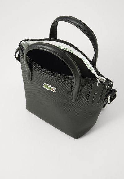 Sac à main noir texturé avec doubles poignées supérieures et fermeture éclair. Présente un logo crocodile vert et une bandoulière détachable pour plus de polyvalence.