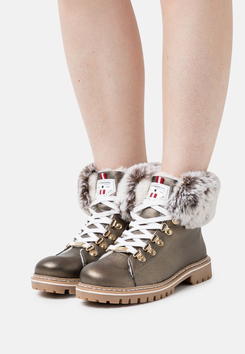 Botas de cuero bronce con cordones, cuello de piel sintética, cordones blancos, herrajes dorados y suela texturizada. Cuenta con un tobillo acolchado para mayor comodidad.