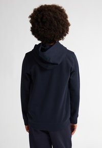 Marineblauwe hoodie gezien vanaf de achterkant, met een gestructureerde stof en geribde mouwen. Eenvoudig ontwerp, zonder zichtbare logo's of patronen.