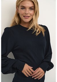Navy blue sweater in a soft knit material with a crew neckline and puffed sleeves. Features ribbed cuffs and subtle seam detailing.