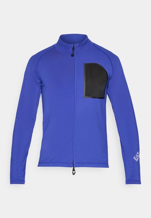 Langermet treningsgenser i lys blå, med en svart glidelåslomme på brystet og stående krage. Laget av glatt, elastisk materiale.