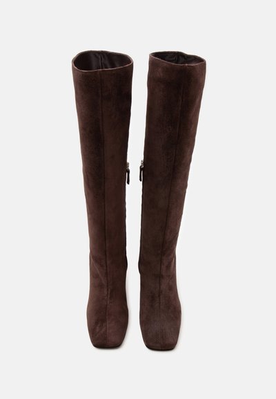 Bottes hautes en daim brun foncé avec fermetures éclair latérales, bouts pointus et coupe slim, présentées debout sur un fond blanc uni.