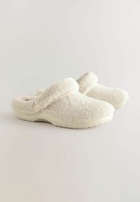 Zuecos de felpa blanca con una textura suave y un diseño de punta redondeada. Con un cuello acolchado y una suela ligera con un agarre estampado.