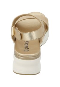 Goldene Leder-Sandale mit einem breiten Riemen und Knöchelverschluss, erhöhter weißer Sohle, glatter Textur und Markenlogo auf der Innensohle.