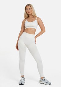 Weißes Sport-BH und hochgeschnittene Leggings, strukturierter Stoff, körperbetonte Passform, dezentes Logo-Detail, kombiniert mit grauen Sportschuhen.
