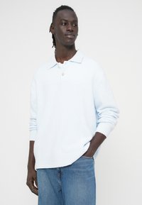 Ανοιχτό μπλε πλεκτό πουλόβερ με απαλή υφή, διαθέτει κλασικό γιακά, πλακέτα με δύο κουμπιά και ριμπ μανσέτες. Φοριέται πάνω από τζιν παντελόνια.