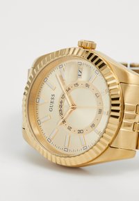 Guld analog ur med tekstureret bezel, en cremet urskive med markante timemarker, datovindue og metal linkarmbånd.