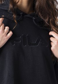 Felpa nera con cappuccio, caratterizzata da un logo FILA in rilievo, realizzata in tessuto morbido e dal taglio comodo. Il design include cordini regolabili e dettagli a coste.