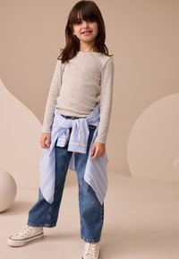 Gray long-sleeve top, blue and pink striped shirt tied at waist, blue denim wide-leg pants, and white high-top sneakers. Smooth fabric textures.