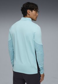 Haut de sport à manches longues bleu clair avec des manches à motif texturé et des accents noirs. Coupe confortable avec un col et un design structuré.