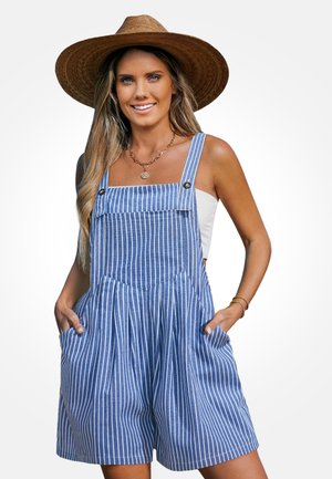 Woman wearing a wide-brimmed straw hat and blue-and-white vertical striped sleeveless romper with pockets, smiling with hands in pockets.