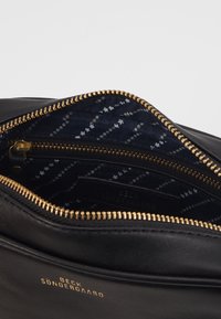 Czarna skórzana torba z złotym zamkiem, z navy wzorzystą tkaniną wewnątrz oraz wewnętrzną kieszonką na zamek, nazwa marki Beck Sondergaard w złotym kolorze.