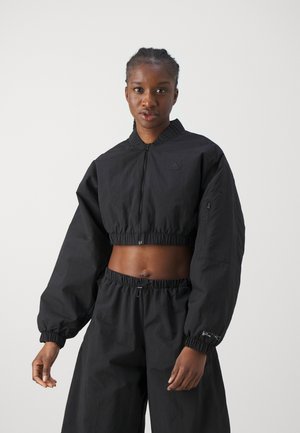 Veste crop noire à manches longues, taille élastique et fermeture éclair à l'avant. Elle présente un petit logo sur la poitrine gauche et un pantalon noir assorti.