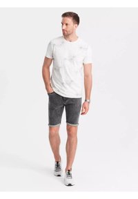 T-shirt blanc avec un motif marbré, associé à un short en denim sombre avec des poignets retroussés, complété par des baskets noir et blanc.