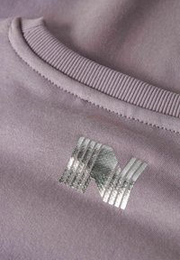 Gros plan sur un tissu lavande avec un col côtelé et un logo abstrait argenté brillant imprimé sur la zone de la poitrine.