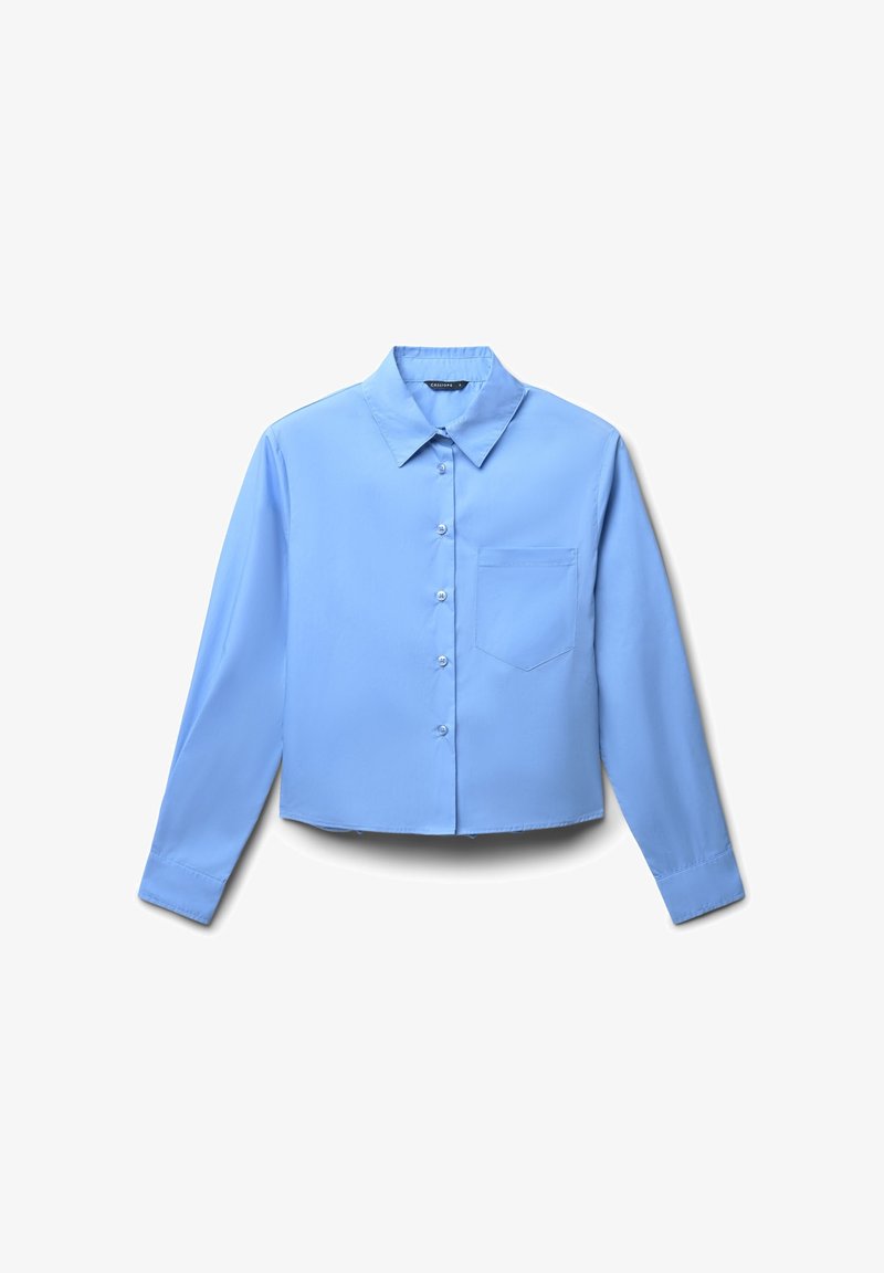 Camicia cropped di colore azzurro chiaro realizzata in tessuto morbido, con colletto a punta, maniche lunghe e una tasca sul petto con chiusura a bottone.