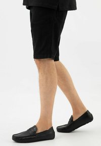 Zwarte leren instapschoenen met decoratieve stiksels, gedragen met zwarte denim shorts, die een relaxte pasvorm en een soepele textuur tonen.