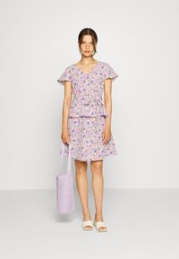Vestido floral com cintura peplum em tons de roxo, rosa e verde; mangas curtas com babados; combinado com uma bolsa em rede lavanda e sandálias bege.