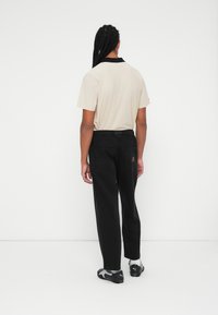 Beige polo shirt med sort krave, parret med sorte bukser med baglommer. Modellen har sorte og grå sportssko på.