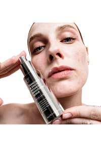 Bottiglia di siero in vetro trasparente con pompa argentata. L'etichetta mostra "Siero Illuminante Avanzato con Tranexamico e Arbutina" in testo bianco.