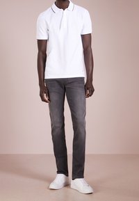 White polo shirt with black collar trim, grey slim-fit jeans, and white sneakers, displayed in a neutral background.
