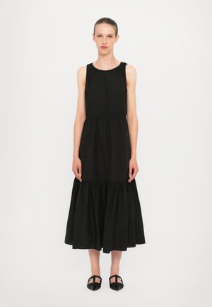 Black sleeveless dress made of cotton with a gathered waist, flowing skirt, and a textured bodice. Worn with black woven shoes.