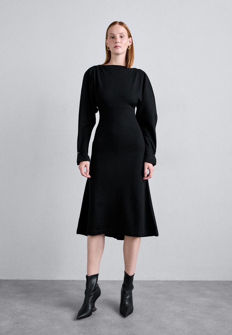 Black long-sleeve dress with a fitted bodice and flared skirt. Made of smooth fabric, features minimal seams and subtle gold accents at the cuffs.