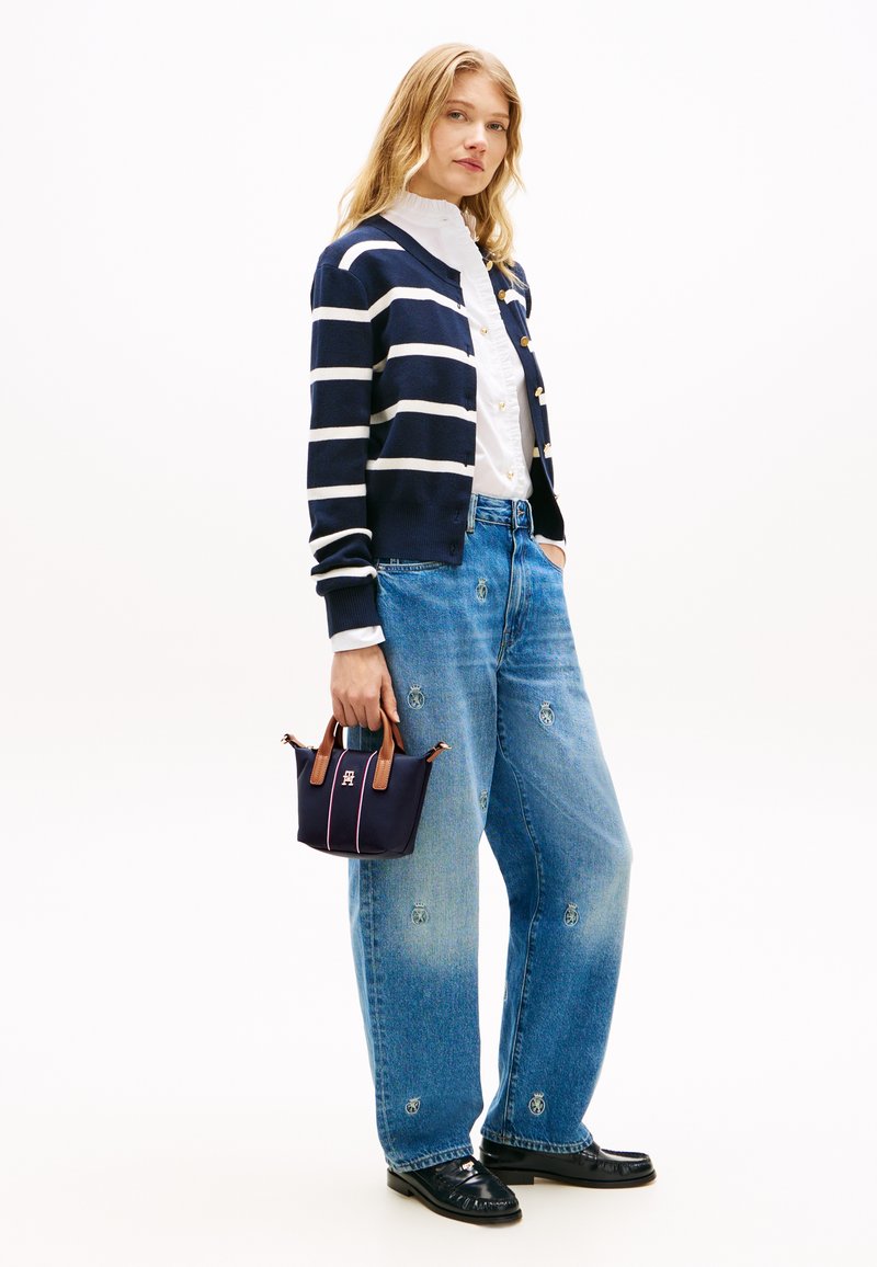 Καρντιγκάν με θαλασσί ρίγες και χρυσά κουμπιά, λευκό πουκάμισο με βολάν, ανοιχτό μπλε τζιν με κεντήματα, και μια μικρή θαλασσί τσάντα με καφέ λαβές και ροζ λεπτομέρειες.