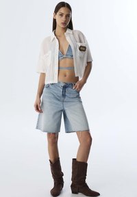 Maglietta bianca a costine con maniche corte, bralette in denim, pantaloni shorts di denim strappati e stivali marroni fino al polpaccio. Materiali texturizzati con una vestibilità casual.