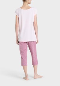 Top corto a maniche corte di colore rosa e pantaloni da pigiama rosa con motivo. I pantaloni presentano un piccolo motivo a cuori e sono di lunghezza cropped, con una texture di tessuto morbido.