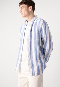 Lichtgewicht gestreepte shirt in blauw en wit linnen, voorzien van een button-down kraag en een enkele borstzak, gedragen over een wit T-shirt.