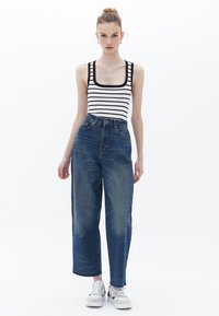 Top a righe bianco e nero con scollatura squadrata, abbinato a pantaloni in denim blu a vita alta, rifiniti con orli sfrangiati e scarpe da ginnastica bianche.