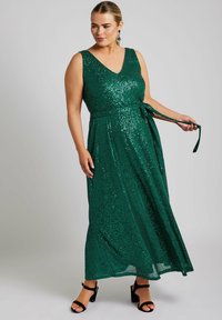 Smaragdgrön paljettmaxiklänning med V-ringning, ärmlös design och knytbart midjebälte. Har en flödande, texturerad yta.
