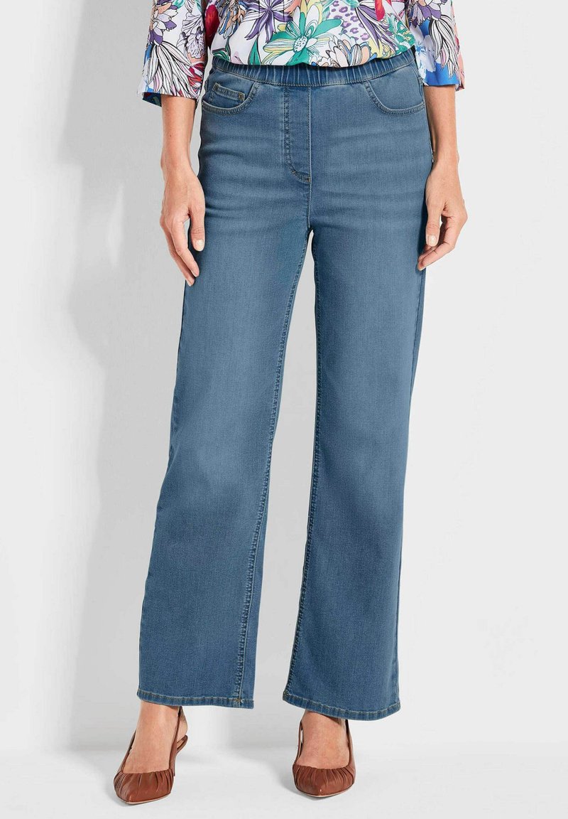 Hellblaue, weit geschnittene Jeans mit glatter Textur, elastischem Bund und vorderen Taschen. Kombiniert mit braunen flachen Schuhen.