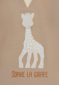 Tessuto beige con un design di giraffe bianche che presenta pois e il testo "Sophie la Girafe" in arancione, posizionato sotto la giraffa.