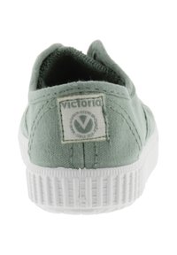 Sneaker in tela verde chiaro vista da dietro, con suola in gomma bianca testurizzata e una toppa in tessuto con il logo sul tallone.