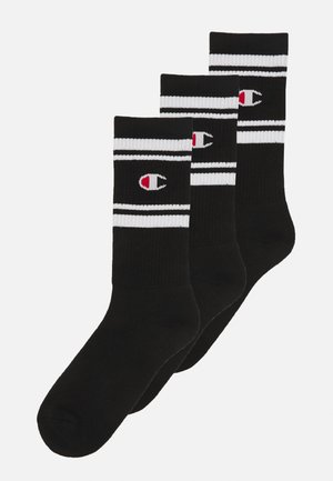Sorte sokker med hvide striber øverst, der har et lille farvet logo på siden. Blød tekstur, ribbet design, solgt i en pakke med tre.