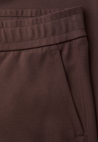 Zbliżenie na ciemnobrązowe spodnie z tkaniny z elastycznym paskiem w talii i detalem bocznej kieszeni, ukazujące fakturę i szwy.