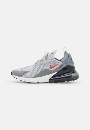 Nike Air Max shoe in gray and white mesh with red accents. Features a prominent air cushioning sole and textured surface.