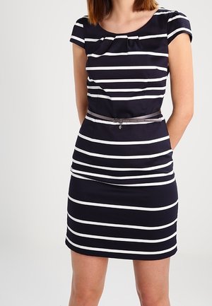 Femme portant une robe noire à rayures horizontales blanches, manches courtes, encolure plissée et une fine ceinture noire à la taille.