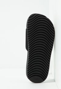 Sort gummisål med et struktureret, ribbet mønster for greb, der har en glat kant og buet form, placeret mod en hvid baggrund.