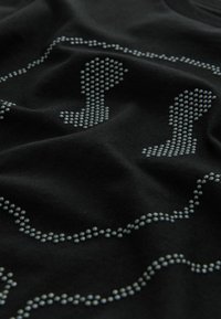 T-shirt nera con un design a pois di colore grigio chiaro. Il tessuto è morbido e strutturato, con una finitura liscia e un look casual.