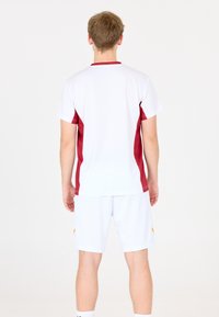 Kortærmet sportsjersey i hvid med maroon sidelækker, parret med hvide shorts med et gult accent på siden.