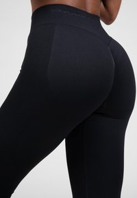 High-waisted black leggings with ribbed texture, seamless design, and branded waistband, featuring a fitted silhouette and smooth finish.