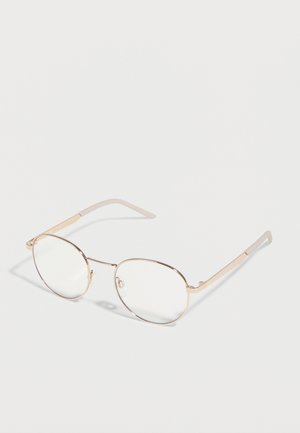 Runde brillerammer i guldmetal med klare linser og beige stangender, vist i en vinkel på en hvid baggrund.